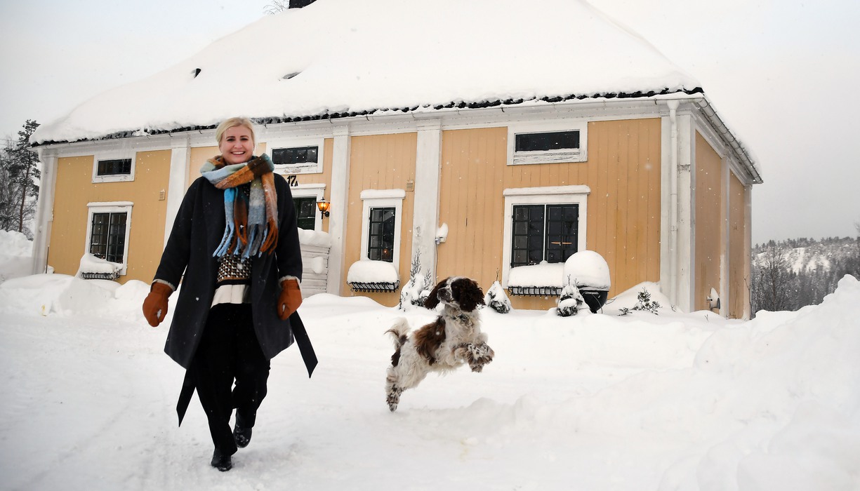en kvinna och en hund går i snön framför ett hus