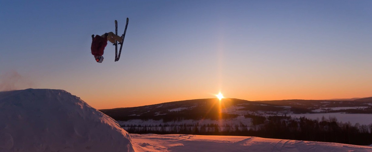 en skidåkare som gör ett hopp med en solnedgång i bakgrunden
