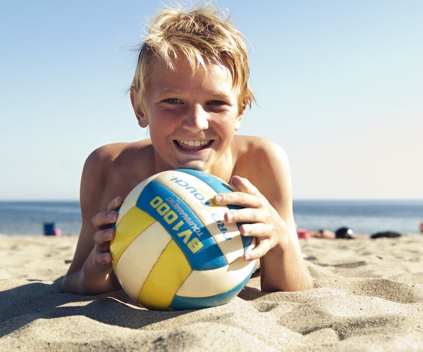 en pojke med en boll ligger på en sandstrand